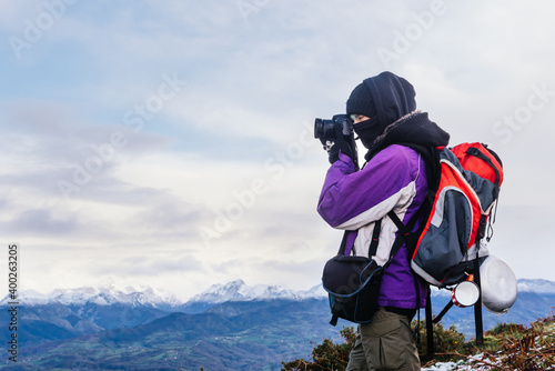 Warmly bundled nature photographer with backpack taking a breather while ascending a mountain. hiker doing a route in winter. sport and free time concept.