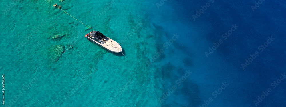 Aerial drone ultra wide photo of speed boat with wooden deck anchored in tropical exotic turquoise crystal clear sea bay Aerial drone ultra wide photo of speed boat with wooden deck anchored in tropical exotic turquoise crystal clear sea bay