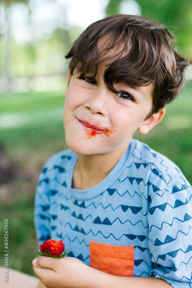 Boy (6-7) eating strawberry in park Boy (6-7) eating strawberry in park