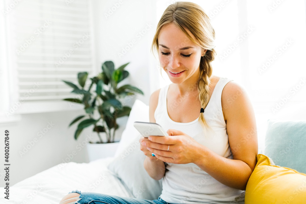 Young woman with mobile phone sitting on bed Young woman with mobile phone sitting on bed