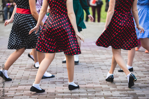 Young women wearing vintage polka dot dresses dancing in city park, close up view of same black dancing shoes and white socks, female retro jazz swing dances, dance lessons