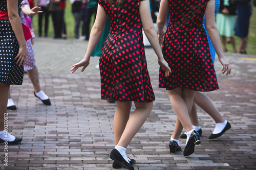 Young women wearing vintage polka dot dresses dancing in city park, close up view of same black dancing shoes and white socks, female retro jazz swing dances, dance lessons