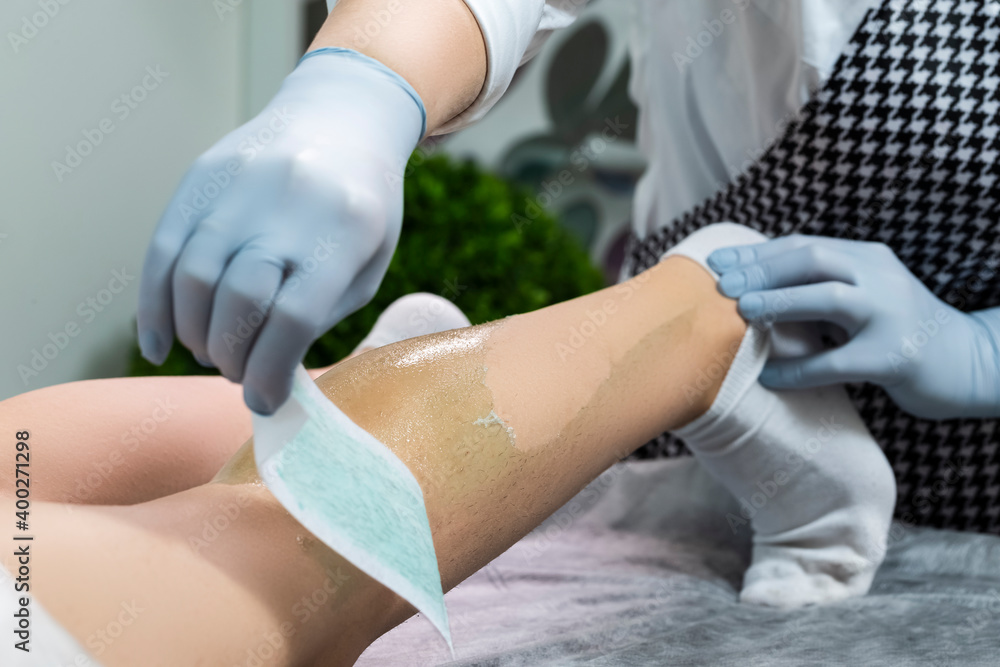 Bodycare Ideas. Macro Close-up of Female Legs Being Treated by Professional Beautician With Sugaring Wax Depilation with Strip in Beauty Salon