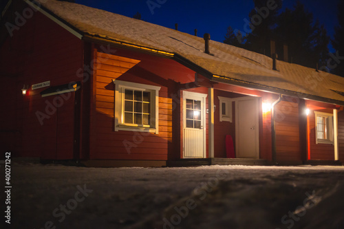 A view of cozy wooden scandinavian cabin cottage chalet house covered in snow near ski resort in winter with the lights on, evening picture