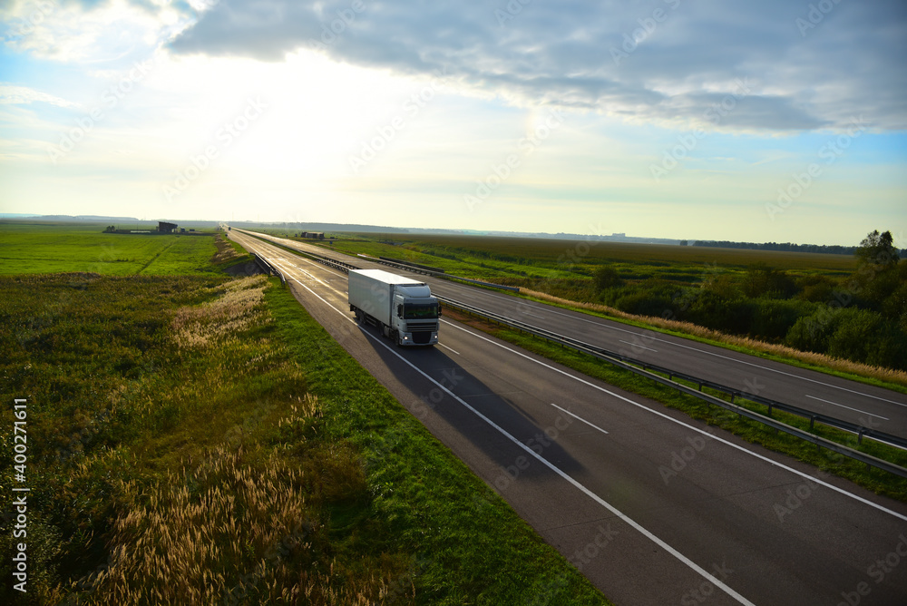 Truck with semi-trailer driving along highway on the sunset background. Goods delivery by roads. Services and Transport logistics. soft focus. Object in motion.