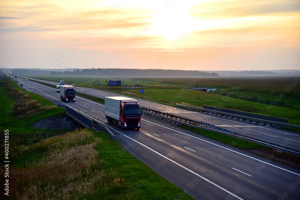 Truck with semi-trailer driving along highway on the sunset background. Goods delivery by roads. Services and Transport logistics. Soft focus. Truck with semi-trailer driving along highway on the sunset background. Goods delivery by roads. Services and Transport logistics. Soft focus.