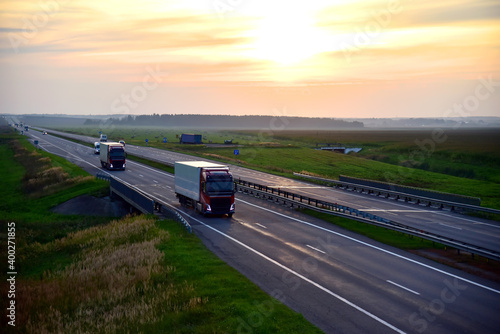 Truck with semi-trailer driving along highway on the sunset background. Goods delivery by roads. Services and Transport logistics. Soft focus.