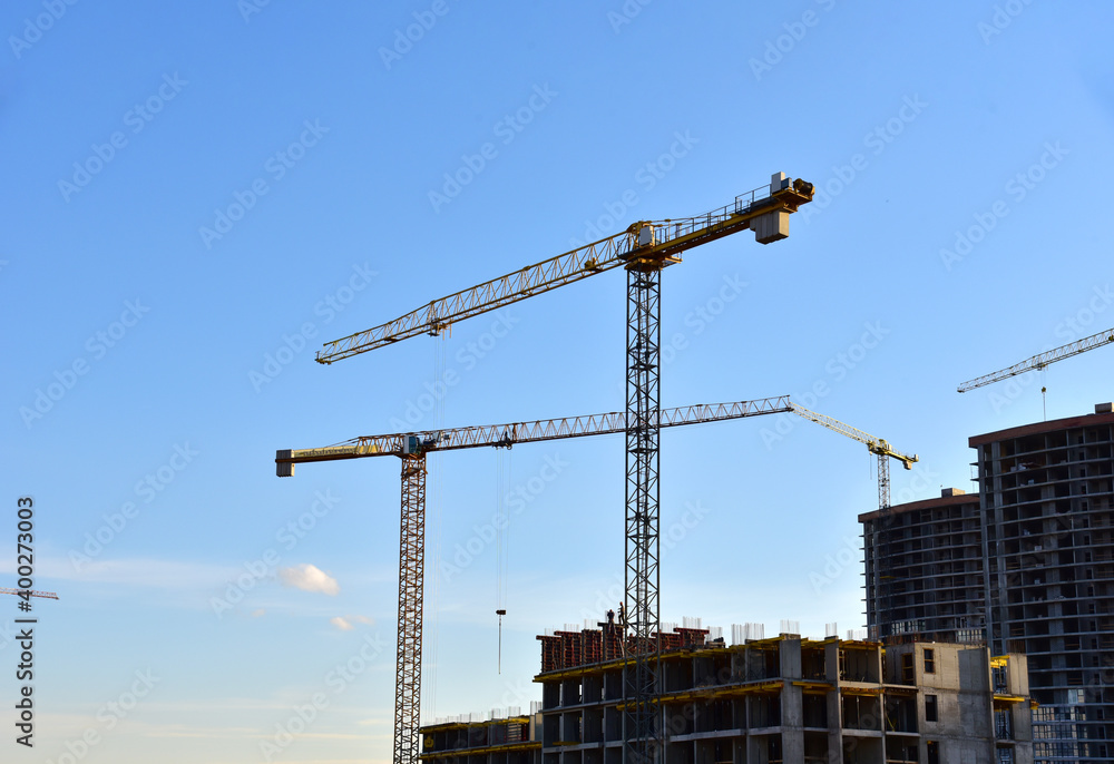 Tower cranes working at construction site on blue sky background. Construction process of the new modern residential buildings Tower cranes working at construction site on blue sky background. Construction process of the new modern residential buildings