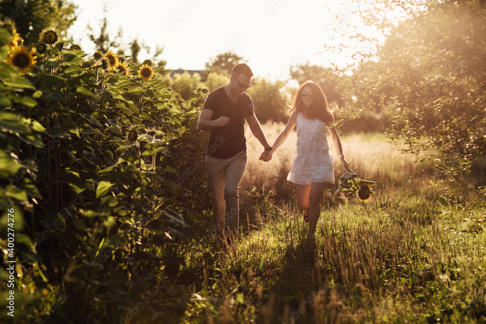 Fototapeta premium Beautiful couple having fun in sunflowers field. A man and a woman in love walk in a field with sunflowers, a man hugs a woman. selective focus
