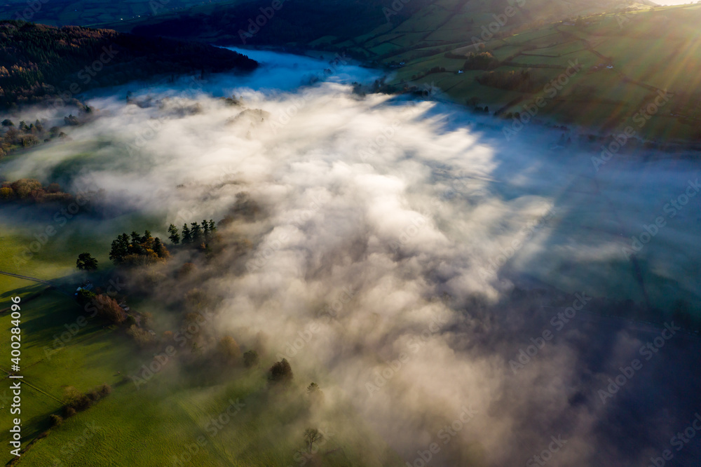 Aerial view of a beautiful valley and hilly rural area filled with fog in late afternoon sunshine