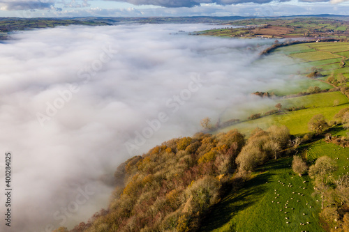 Aerial view looking down onto rural farmland and a valley filled with a blanket of fog (Wales)