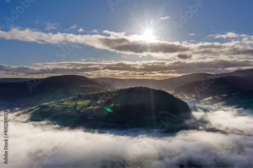 Aerial view of a beautiful valley and hilly rural area filled with fog in late afternoon sunshine