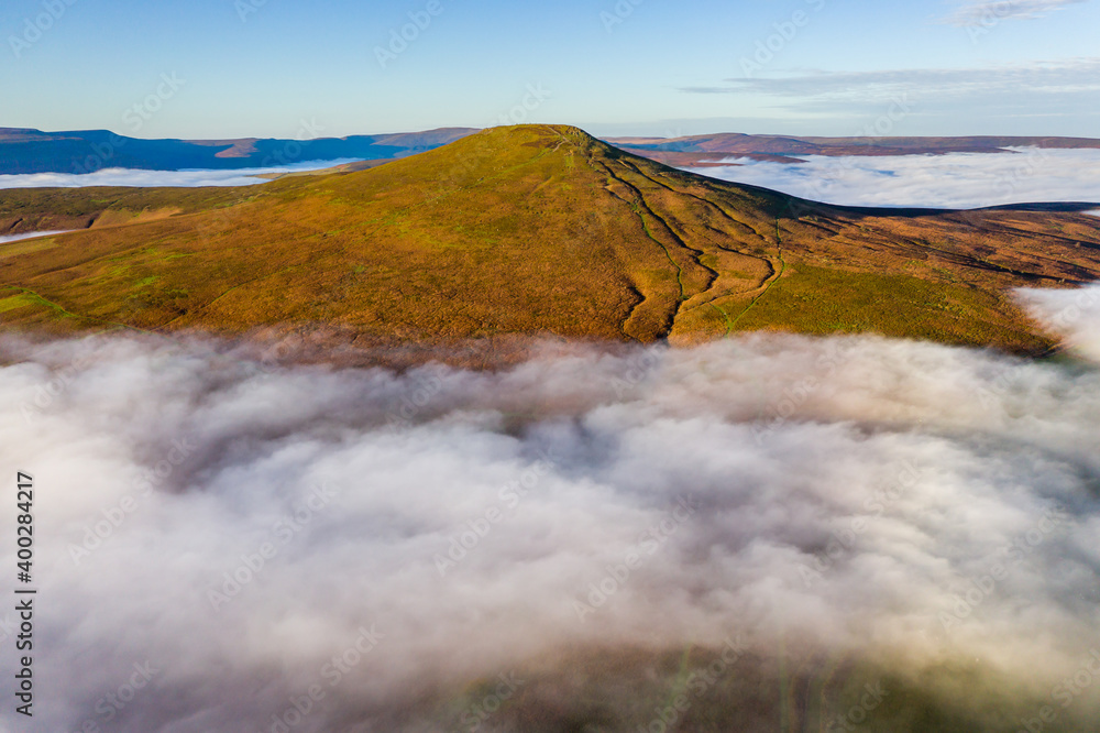 Aerial view of a mountain peak rising above a sea of low cloud and fog in the valley below (Sugar Loaf, Wales)