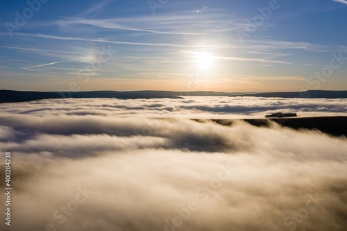 Aerial view of the sun setting above a sea of fog and low cloud