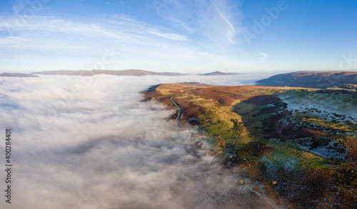 Aerial panorama of a narrow, winding mountain road emerging above a bank of fog in a rural valley