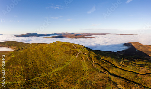 Panoramic aerial view of a mountain summit rising above a sea of low cloud and fog (Sugar Loaf, Wales)