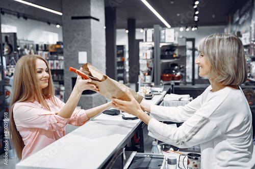 Woman examines various items of dishes. Beautiful woman shopping tableware in supermarket. Manager helps a costumer. photo