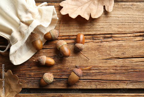 Acorns and oak leaves on wooden table, flat lay. Space for text