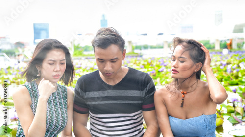 Three asian young friends seated on a bench looking at something on the laptop
