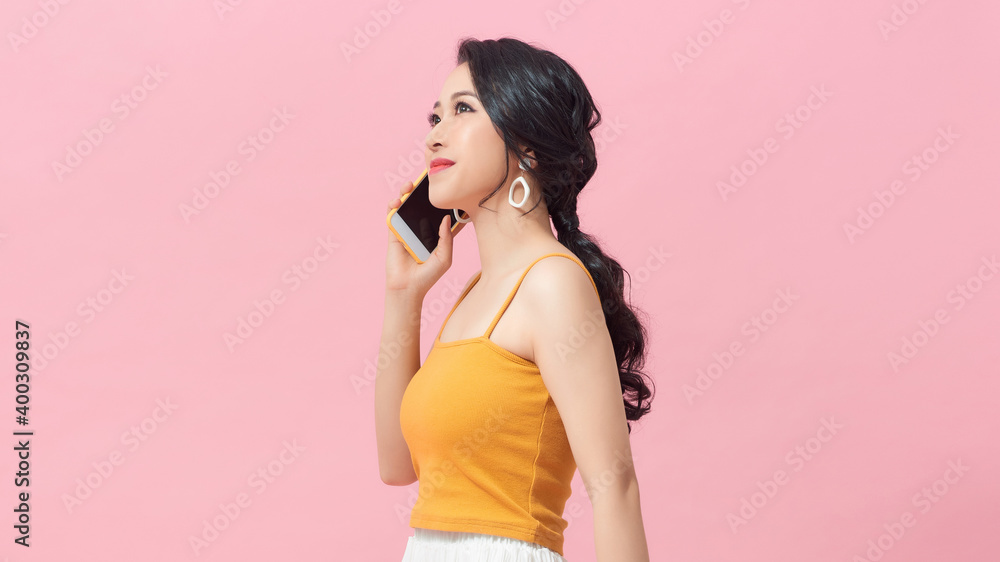Happy asian woman in casual clothes talking by smartphone and looking away over pink background Happy asian woman in casual clothes talking by smartphone and looking away over pink background