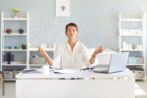 Fototapeta Tired woman sitting in office practicing meditation technique for concentration