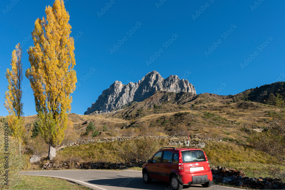 Red car running in small road with yellow poplar tree and mountain peak background in Spain