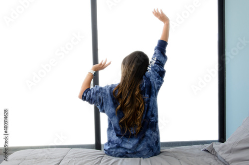 Vista trasera de mujer estirando los brazos en la orilla de la cama viendo hacia la ventana por la mañana. photo