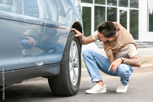 Fotografia Handsome man checking tires of modern car