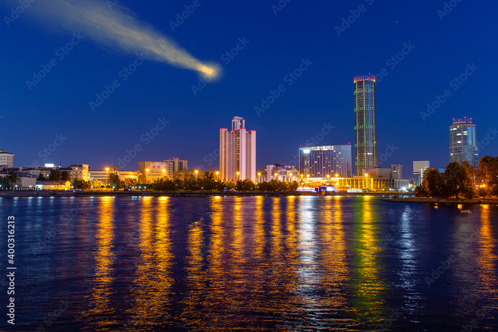 Naklejka premium Comet in the night sky above the city skyscrapers. Reflection in the river