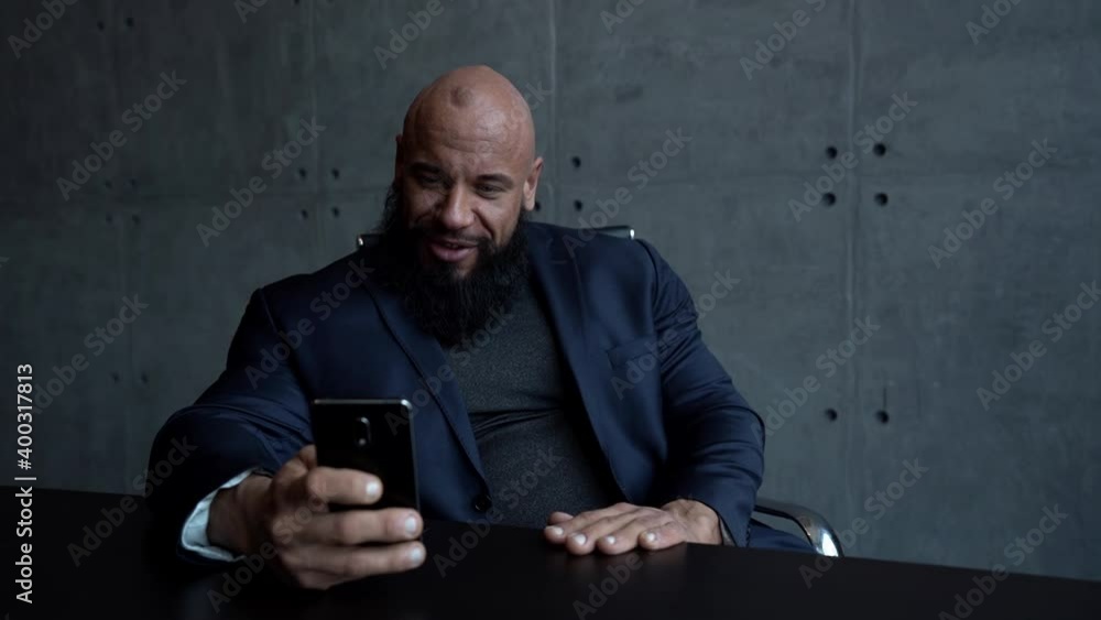 cheerful bald man dressed black jacket is sitting in home office and chatting by video call at smartphone cheerful bald man dressed black jacket is sitting in home office and chatting by video call at smartphone