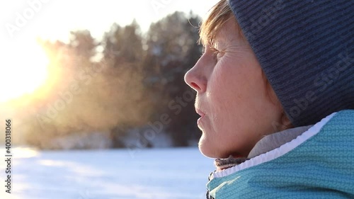 Young woman blows steam from her mouth on a sunny winter day