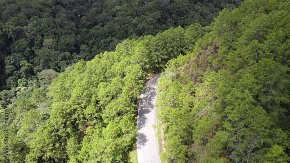 Aerial view of a car running along the mountain road through tropical forest in countryside by drone Aerial view of a car running along the mountain road through tropical forest in countryside by drone