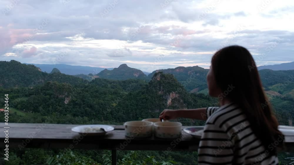 An asian woman eating food while sitting on balcony with greenery mountains view An asian woman eating food while sitting on balcony with greenery mountains view