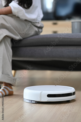 Robotic vacuum cleaner cleaning the living room and woman sitting on sofa at home.