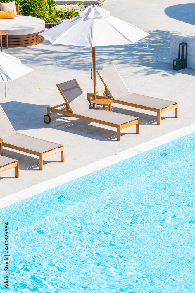 Umbrella and deck chair around outdoor swimming pool in hotel resort - obrazy, fototapety, plakaty 