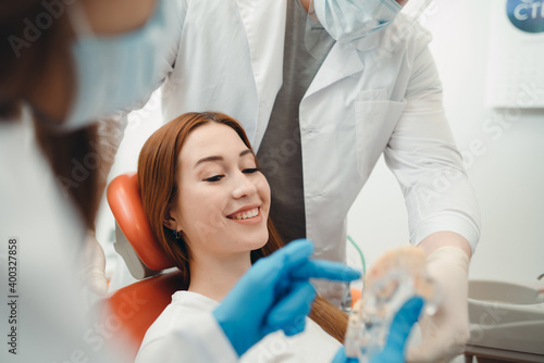 Woman with red hair sits in a dental chair while doctors demonstrate teeth cast
