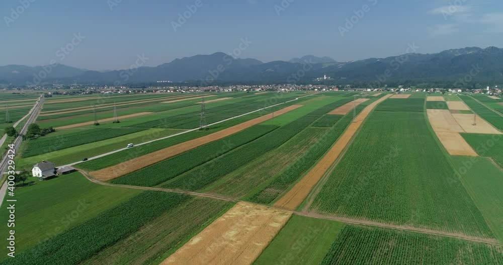 Aerial drone view of farming grassland fields, Slovenia. Elevated view of flatland farmland. Straight railway railroad between agriculture fields. Small village and mountains in the distance Aerial drone view of farming grassland fields, Slovenia. Elevated view of flatland farmland. Straight railway railroad between agriculture fields. Small village and mountains in the distance
