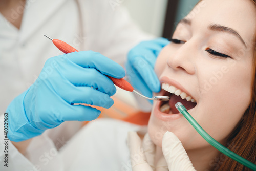 Portrait of a beautiful woman with an open mouth next to which hands in gloves holding dental instrument