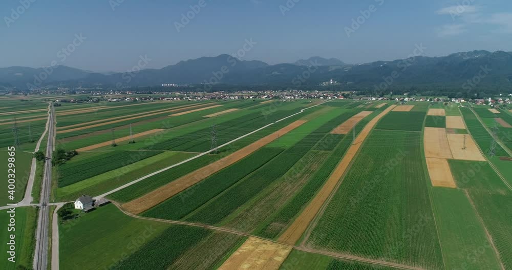 Aerial drone view of farming grassland fields, Slovenia. Elevated view of flatland farmland. Straight railway railroad between agriculture fields. Small village and mountains in the distance Aerial drone view of farming grassland fields, Slovenia. Elevated view of flatland farmland. Straight railway railroad between agriculture fields. Small village and mountains in the distance