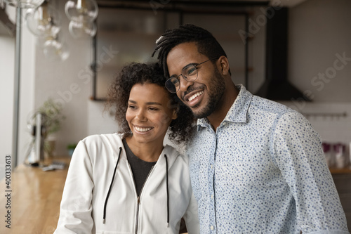 Smiling millennial African American couple hug look in distance dreaming planning future together. Happy young biracial man and woman renters or tenants imagine or visualize family opportunities.