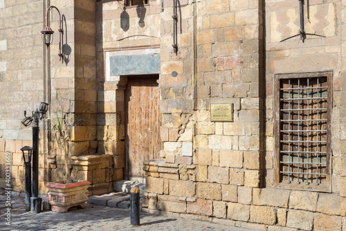 Entrance of historic ottoman era theological school named Madrasa El Ainy with wooden door and decorated wrought iron window over stone bricks wall, located at Azhar district, Medieval Cairo, Egypt