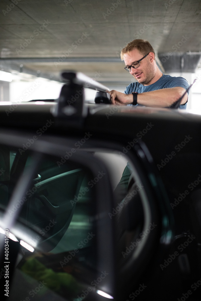 Handsome young driver getting ready to go biking - putting a bike rack on the roof of his car