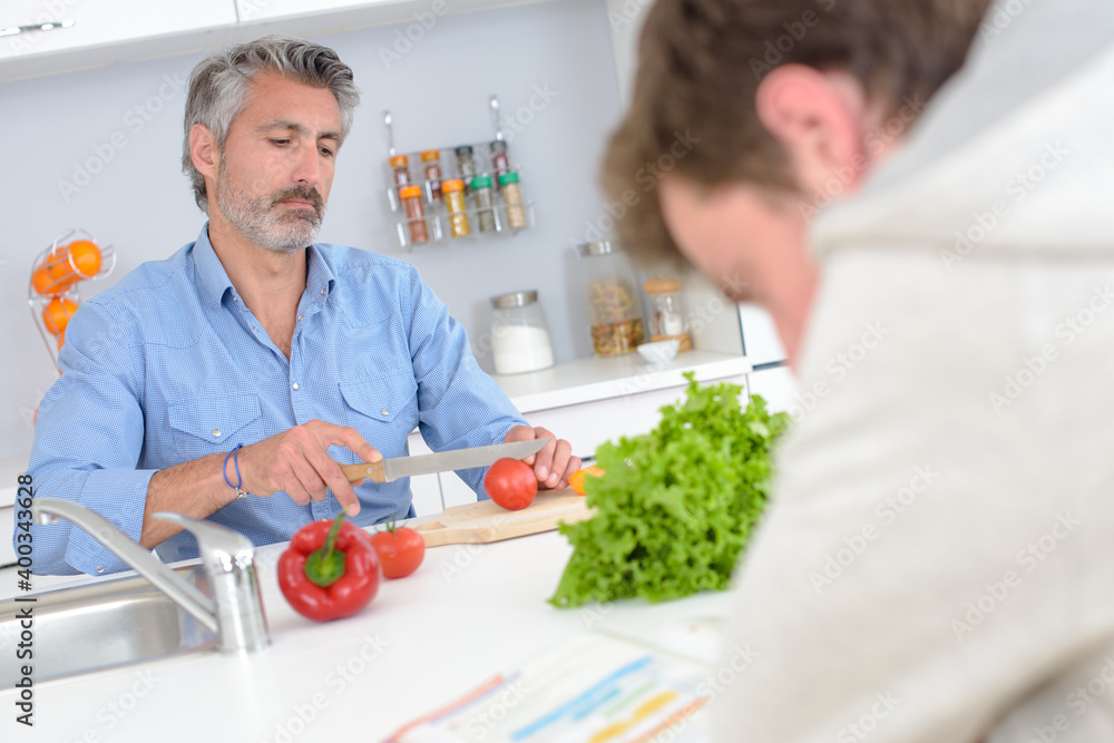 Man preparing vegetables while boy reads book Man preparing vegetables while boy reads book