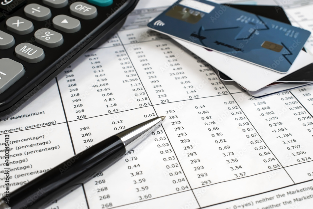 on the financial documents is a pen near the calculator on a blurry background of credit cards. Business and financial concept on the financial documents is a pen near the calculator on a blurry background of credit cards. Business and financial concept