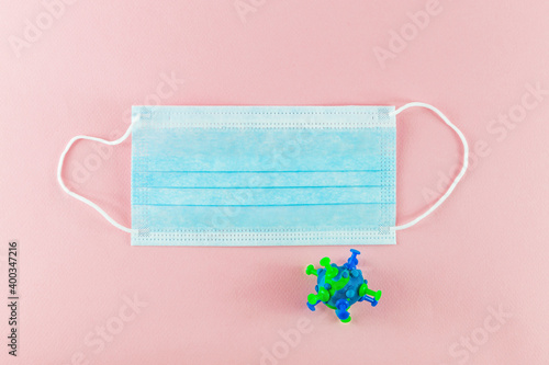 Therapeutic  surgical mask for protection against flu and other viral diseases, with a model of a coronavirus bacterium made of plasticine. Protective mask on a pink paper background against the sprea photo