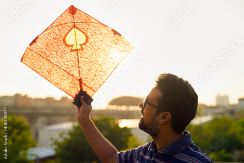 Young man holding aloft colorful paper and wood kite against a blurred background setting sun on the indian kite festival of makar sankranti or uttarayana photo