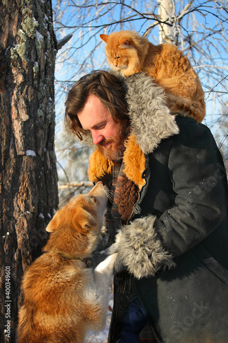 a bearded man with a red cat on the background of a winter forest