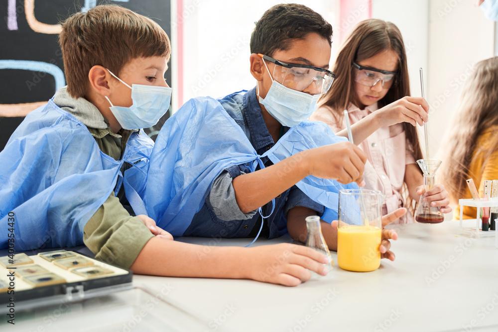 Obraz premium Two curious boys in protective masks and gowns mixing liquids