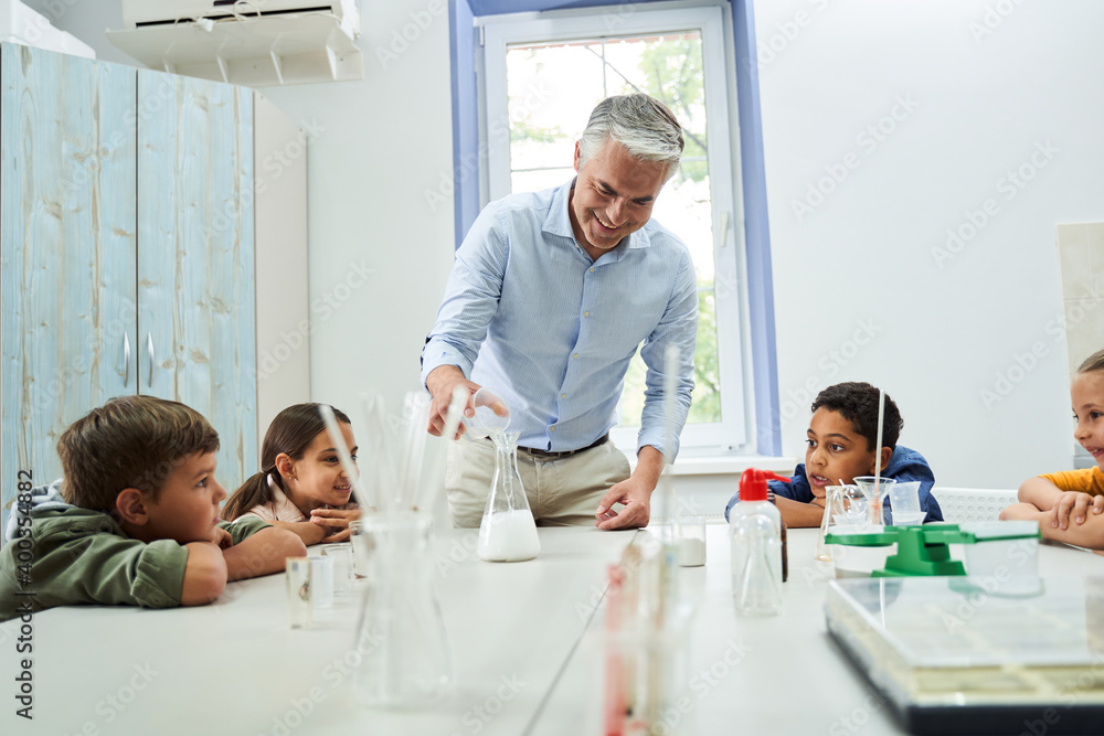 Obraz premium Children looking with interesting at their handsome grey haired teacher