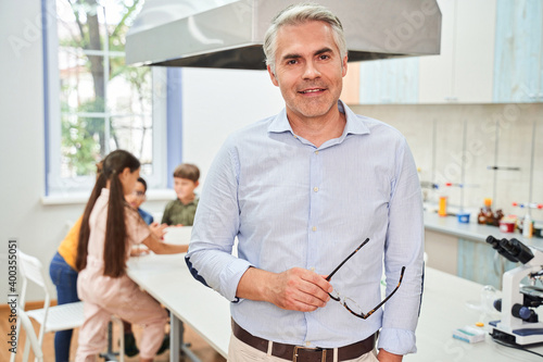 Senior handsome grey haired teacher holding glasses